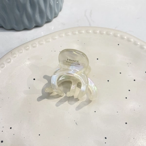 Close-up of a mini acetate octopus hair claw in iridescent white on a ceramic tray