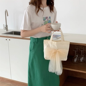 Nahaufnahme der cremefarbenen Canvas-Handtasche mit großer gelber Netzschleife als Detail