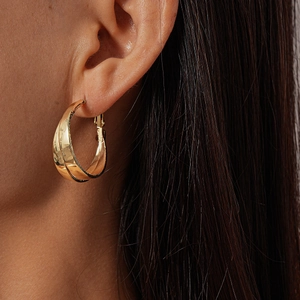 Side view close-up of a high-polish gold C-shaped hoop earring worn on an ear
