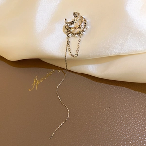 Détail d'un ear cuff doré à pampilles avec petites perles blanches et strass brillants