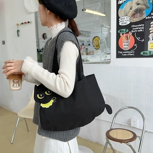 Asian model carrying a black canvas tote bag with yellow cat embroidery in a cafe