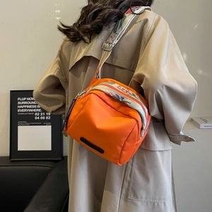 Orange nylon shell crossbody bag with colorful patterned wide strap shown on model
