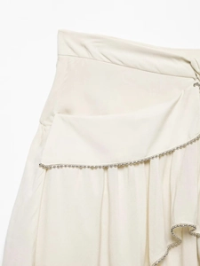 Detailed view of cream ruffled mini skirt featuring intricate silver bead trim craftsmanship