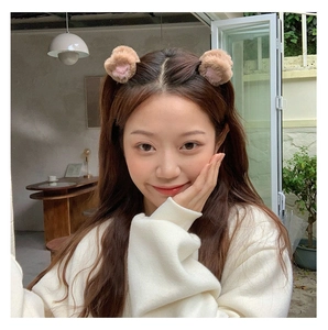 Brown plush bear ear hair clips worn by a model in a cozy natural cafe setting