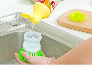 Filling soap dispenser handle of the green kitchen scrubbing brush over a sink