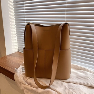 Detail einer braunen Leder-Eimertasche mit breitem Gurt auf hölzerner Oberfläche