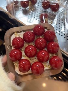 Macro detail of glossy red resin cherry earrings with gold hooks in a wooden display tray