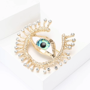 Detail shot of a gold metal evil eye brooch with sparkling rhinestones and blue enamel inlay