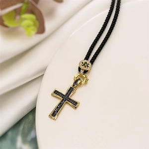 Detailed macro view of gold-plated cross pendant with black zircon pavé and woven cord