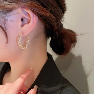 Close-up of a gold geometric C-shaped hoop earring with inset zircon stones on a model
