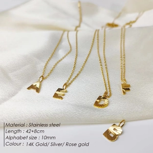 Detailed macro view of 14K gold plated stainless steel letter pendant on white silk fabric