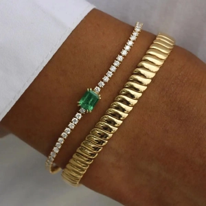 Close-up of a 10mm gold tennis bracelet with emerald green gem and textured bangle