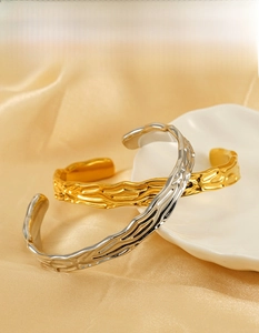 Detail of irregular textured 18k gold plated stainless steel bangles on satin