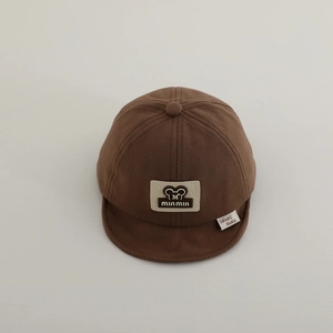 Dettaglio del cappellino marrone scuro per neonati con visiera morbida e toppa a fumetto