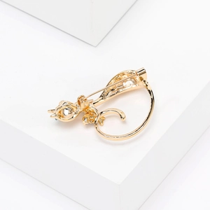 Elegant gold cat brooch with sparkling rhinestones and green gem on a white background