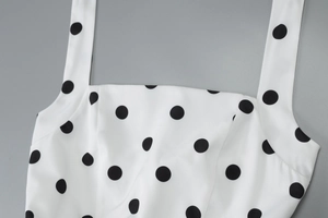 Close-up of a white dress with black polka dots featuring square neckline and fixed straps