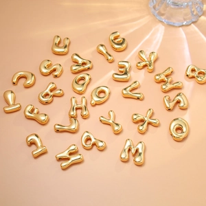 Macro shot of 18K gold-plated bubble alphabet beads on a peach background