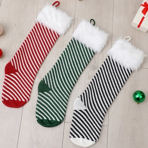 Three knitted Christmas stockings with plush fur trim and striped patterns on wood floor