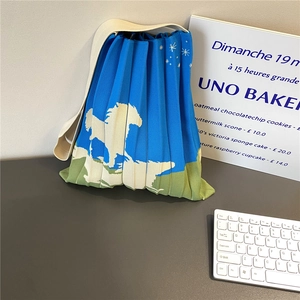 Detail of blue knitted pleated tote with sky and horse pattern on a minimalist desk