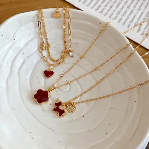 Gold-plated pony necklace set with red clover and zircon heart charms in a ceramic dish