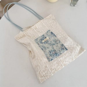 Close-up of cream canvas tote bag with blue lace floral pocket and elegant lace texture