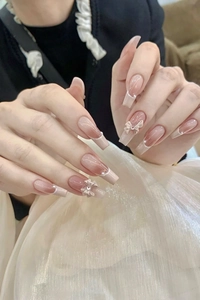 French press-on nails with nude pink gradient, white bows, and elegant pearl accents