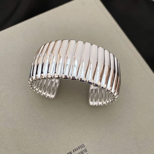 Detail of silver metallic wide open cuff bracelet with rhythmic 3D wavy textured surface