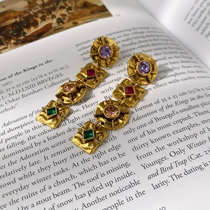 Detail of vintage gold earrings with colorful gemstones on an antique book page