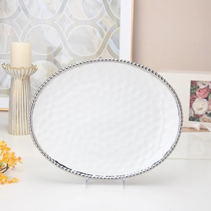 Detail of white oval ceramic plate featuring silver beaded edges and hammered texture