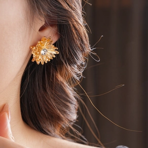 Detail of gold flower stud earring with crystal center worn on model's ear