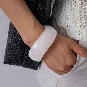 Macro detail of wide acrylic bangle featuring white marble texture on a woman wrist