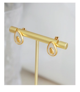 Macro detail of avocado-shaped stud earrings with gold finish and white enamel inlay