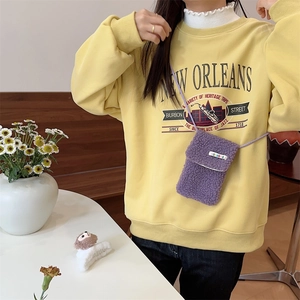 Detail of purple faux shearling mini crossbody phone bag on a mustard yellow sweatshirt