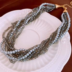 Detail of multi-layered pearl and crystal necklace with golden clasp on white plate