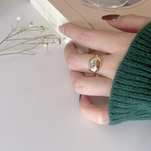 Dettaglio anello dorato con zircone rettangolare indossato da una modella in maglia di lana