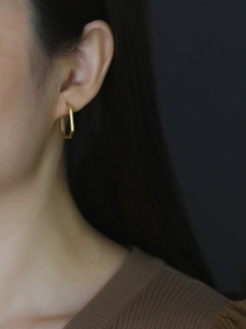 Close-up of elegant gold square hoop earring worn by a model with a dark background