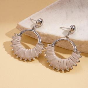 Detail of silver metal earrings with beige woven leather on elegant marble base