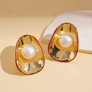 Boucles d'oreilles dorées avec grandes perles et accents rouges sur présentoir pierre