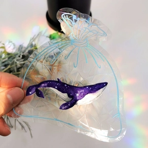 Detail of a transparent holographic money bag sticker featuring a purple whale embroidery