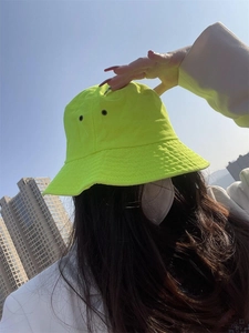 Neon green cotton bucket hat with breathable eyelets worn by a model against city sky