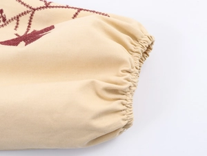 Detail shot of beige sleeve cuff with intricate burgundy floral vine embroidery
