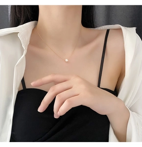 Close-up of minimalist gold necklace with a natural white pearl on a female model