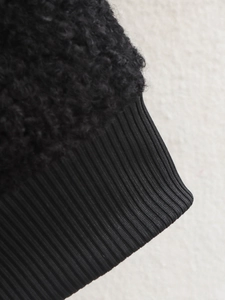 Macro detail of black sherpa fleece fabric and ribbed knit cuffs on a bomber jacket