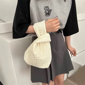 Off-white pleated canvas wrist bag with textured fabric shown on a model wrist