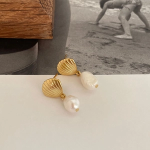 Golden shell earrings with white pearl pendants displayed on a minimalist background