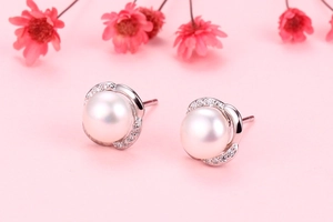 Detail view of crown pearl stud earrings with sparkling stones on a pink background