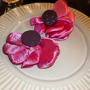 Detail of rose red satin flower earrings with pearl stamen on a white ceramic tray