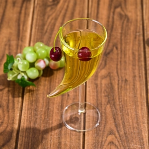 Unique curved horn-shaped cocktail glass with yellow drink and red cherries on dark wood