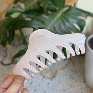 Close-up of large pastel pink claw clip held against a monstera leaf and terrazzo background