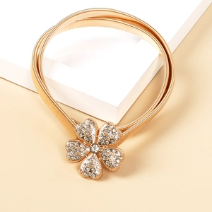 Detail eines champagnergoldenen elastischen Metallgürtels mit funkelnder Strass-Blumenschnalle